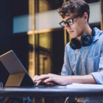 Young,Handsome,Concentrated,Man,In,Glasses,With,Headphones,Browsing,Ultrabook